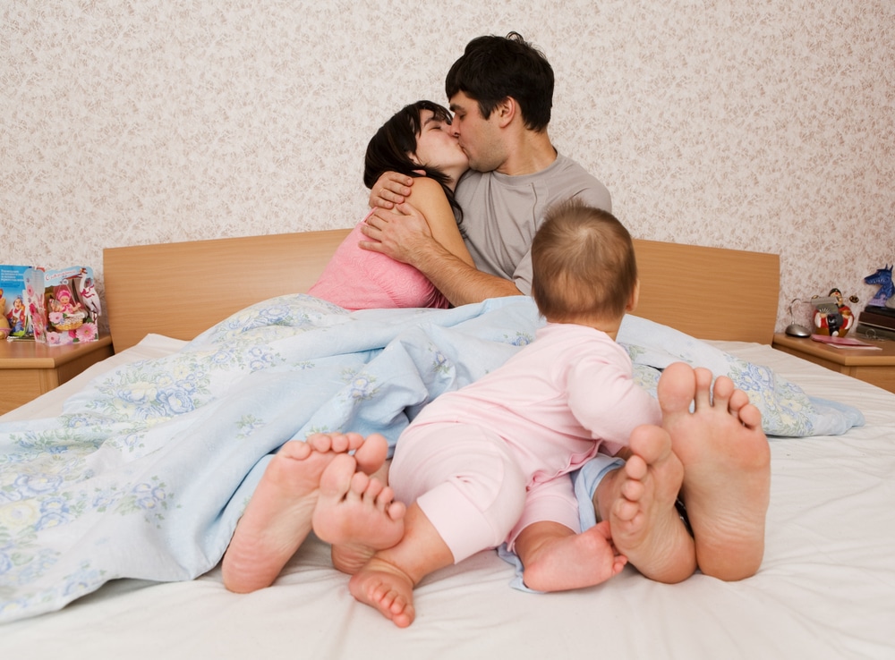 parents kissing in bed with baby